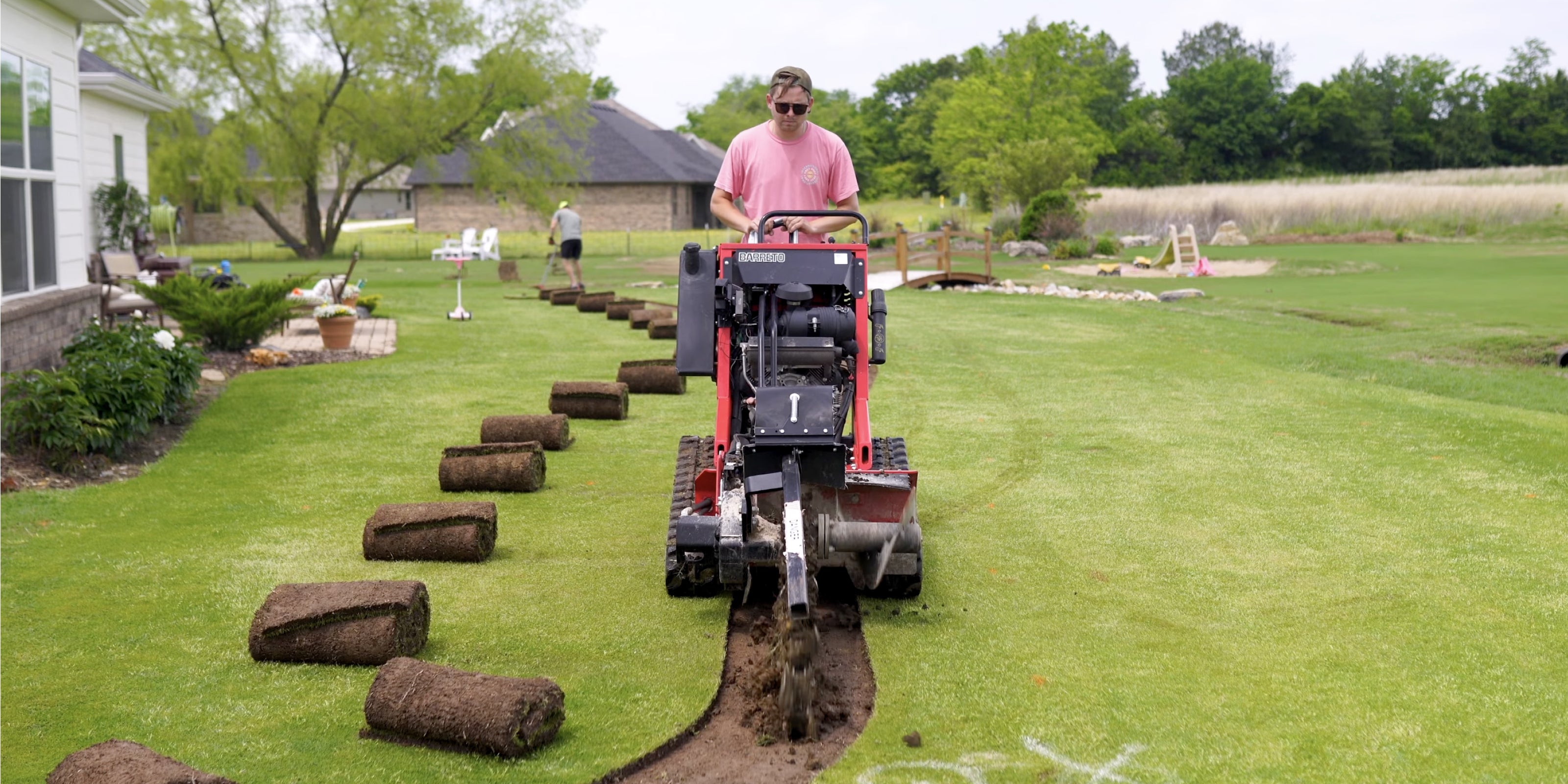 Trenching machine cutting narrow trench in well-maintained lawn with rolled sod set aside for Irrigreen install
